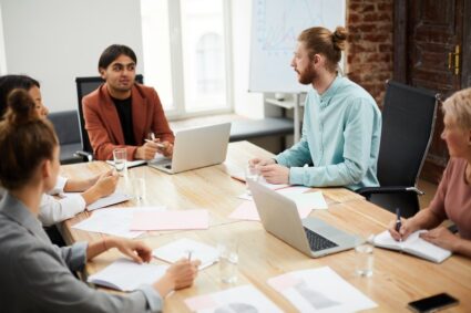Portrait of young Middle-Eastern businessman talking to colleagues sitting at meeting table and discussing projects, copy space