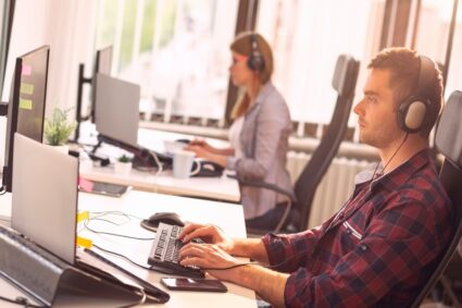 IT support team working in an office; call centre operators wearing headsets and typing on a computer keyboard, receiving calls